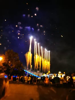 Brilliant fireworks burst into vibrant colors above a lively waterfront as excited spectators gather to celebrate an evening event under the night sky.