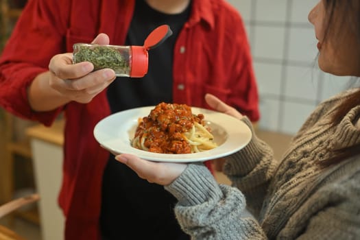 Close up of man sprinkling herbs on spaghetti bolognese before serving.