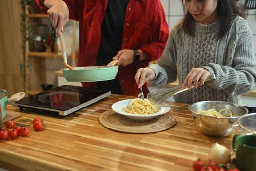 Happy couple preparing a delicious pasta dish for festive dinner.