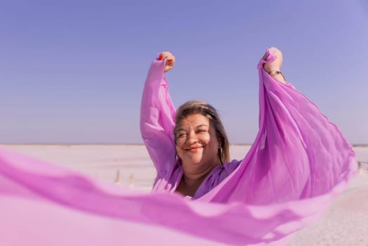 A woman in a pink dress twirls and smiles, her arms raised as she holds the fabric of her dress in the wind. The background is a white landscape.