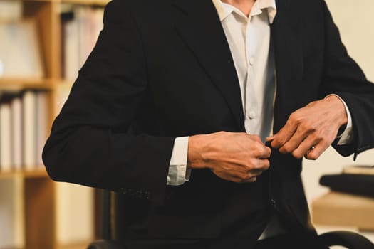 Executive businessman buttoning his jacket while standing in modern office.
