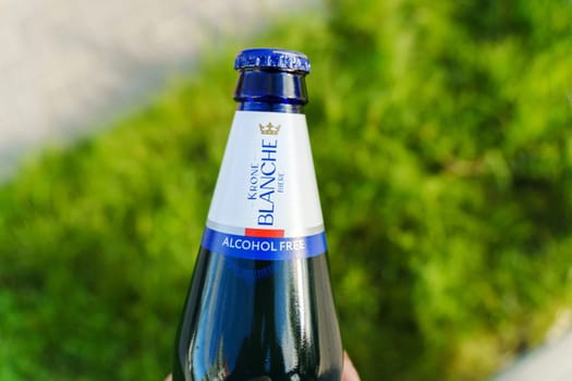 Tyumen, Russia-August 10, 2024: hand grasps a chilled bottle of alcohol-free Krone Blanche while sitting on a swing in a sunny park