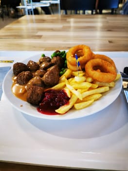 A plate features meatballs drizzled with savory sauce, accompanied by crispy fries, onion rings, and a dollop of red sauce. This appetizing meal is ideal for a relaxed lunch.