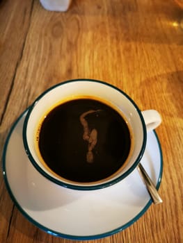 This cup of black coffee, placed on a rustic wooden table, reveals unique swirls and patterns created by the brew, inviting a moment of enjoyment.