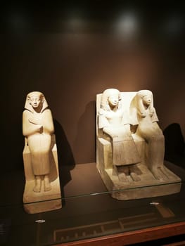 Two ancient sculptures represent Egyptian artistry, featuring one standing figure and two seated ones, highlighting the culture's reverence for form and style in a museum setting.