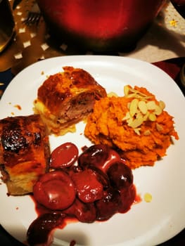 A holiday meal showcases stuffed meat rolls beside creamy sweet potato mash topped with almonds and a rich cherry sauce, celebrating warmth and flavor together.
