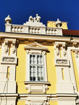 The vibrant yellow facade of a beautifully detailed building features exquisite architectural elements, highlighting the artistry of historical European design against a clear blue sky.