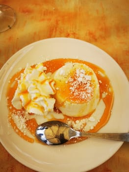 A creamy dessert sits on a plate, drizzled with caramel sauce and surrounded by a dollop of whipped cream and powdered sugar, inviting sweet indulgence.