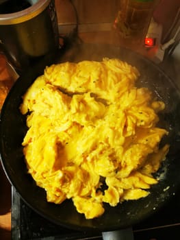 A cozy kitchen is filled with warmth as scrambled eggs are being cooked in a frying pan, surrounded by spices and an inviting atmosphere during dinner preparation.