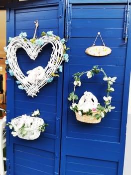 A charming spring display showcases white bunnies nestled in floral arrangements, hanging from a vibrant blue wooden backdrop, creating a festive atmosphere.