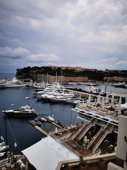 Numerous elegant yachts line the marina in Monaco during a cloudy afternoon. The bustling harbor reflects the luxury lifestyle of the area, with stunning buildings in the background.