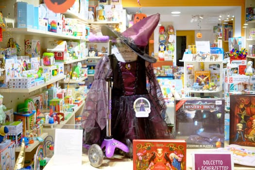 Cremona, Lombardy, Italy - October 31st 2024 A captivating halloween display showcasing a witch costume and a purple scooter in a toy store window, adorned with festive decorations