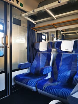 The interior of a train carriage features blue patterned seats, with sunlight illuminating the empty space and highlighting the contemporary design.