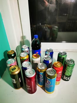 A variety of beverage cans and a bottle positioned on a windowsill, showcasing different colors and labels in a cozy, brightly painted room.