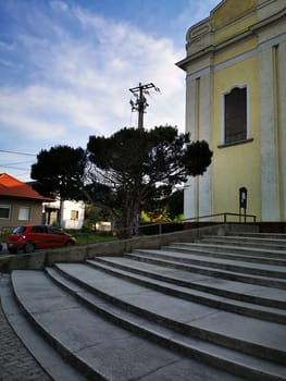 The image showcases a set of stone steps leading to a yellow historic building. In the background, residential homes and a power line can be seen beneath a bright sky.