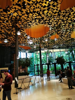 Large windows reveal lush greenery outside while visitors wander through a contemporary art gallery with striking geometric patterns overhead.