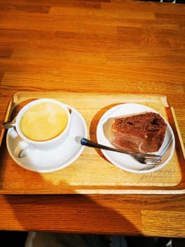 A warm cup of coffee accompanied by a generous slice of chocolate cake sits elegantly on a wooden tray. The inviting atmosphere enhances the delightful experience.