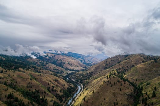 The sky is cloudy and the mountains are covered in trees. The landscape is beautiful and peaceful. The clouds give the scene a sense of calmness and serenity