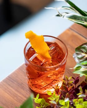 Negroni cocktail is standing on a table with an orange peel garnish