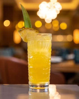 Refreshing pineapple cocktail served in tiki-style glass standing on bar with blurred restaurant background