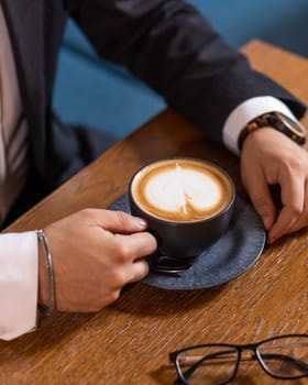 Businessman enjoying a coffee break, holding a cup of cappuccino with latte art on a wooden table