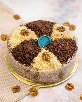 Round cake with chocolate and walnuts, decorated with a blue round tag on top, sitting on a golden cardboard