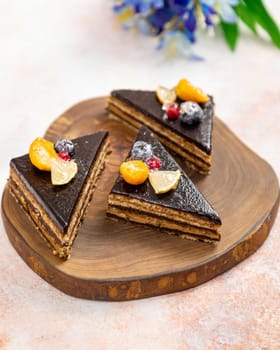 Chocolate cake slices topped with chocolate ganache, physalis, blueberries and lemon slices, laying on wooden board
