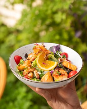 Waiter is holding a bowl of salmon and shrimp salad with orange slices and microgreens