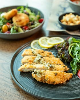 Sliced breaded chicken breast served with lemon and salad on a restaurant table