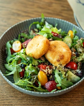 Fresh salad with fried goat cheese, tomatoes, strawberries, blueberries, arugula and walnuts served on wooden table