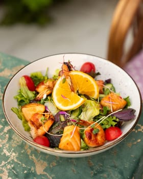 Fresh salad with grilled salmon and shrimps is served on a white plate decorated with a slice of orange