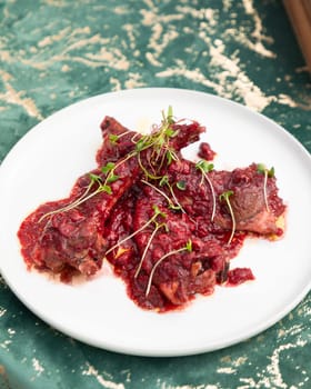 Delicious roasted lamb ribs with cranberry sauce decorated with microgreens on white plate on green tablecloth