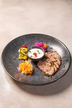 Sliced roast beef with herbs and spices served on a plate with pickled vegetables and a creamy sauce, creating a visually appealing and flavorful culinary experience