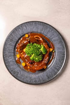 Delicious roast beef with broccoli and potatoes lying on plate decorated with herbs on light background