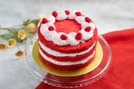 Delicious red velvet naked cake with raspberries on top, sitting on a glass cake stand