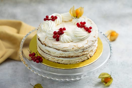 Freshly baked meringue cake decorated with whipped cream, redcurrant and physalis on a gray background