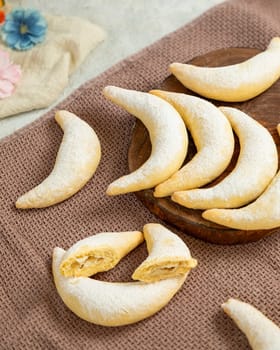 Crescent shaped cookies with filling covered with powdered sugar lying on brown cloth