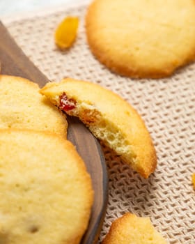 Round cookies with candied fruit are lying on a wooden board and a beige napkin, one of them is broken in half