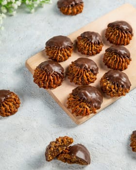 Delicious chocolate covered oatmeal cookies laying on a wooden board on a white surface