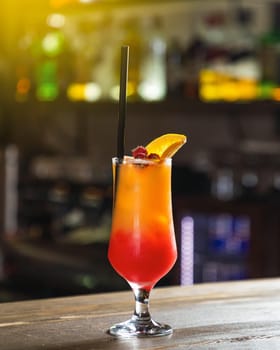 Colorful cocktail is standing on the bar counter with a blurry bar background
