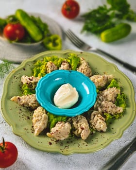Steamed manti dumplings seasoned with red pepper flakes served on a green plate with sour cream, a staple of central asian cuisine