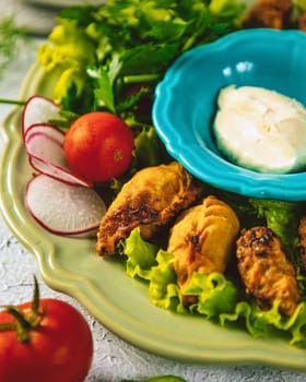 Fried gyoza dumplings are served on a green plate with a side of dipping sauce and fresh vegetables
