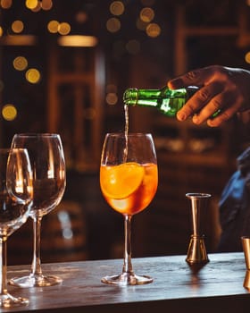 Bartender is pouring an alcoholic drink into a cocktail glass containing ice cubes and orange slices