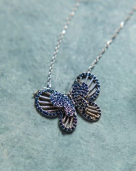 Silver necklace with blue gems forming a butterfly shape, placed on a blue background