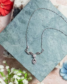 Elegant silver necklace with diamonds resting on a blue stone and surrounded by flowers