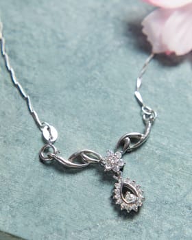 Elegant silver necklace with diamonds on blue background decorated with flower petals