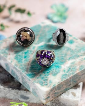 Three gemstone rings with diamonds sparkling on a green marble slab