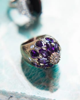 Gold ring with purple amethyst and diamonds on turquoise background, ideal for showcasing luxury and elegance
