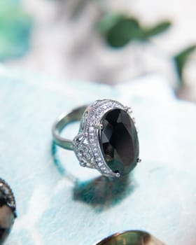Silver ring with black gemstone and diamonds on light blue background with blurred green leaves