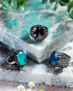 Silver men's rings with black, blue and green gemstones on a turquoise background